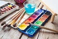 Box of watercolor paints, art brushes, glass of water and easel Royalty Free Stock Photo