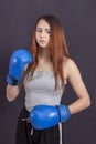 Boxer girl in blue boxing gloves in a gray t-shirt in rack