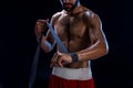 Boxer preparing her gloves for a fight. Photo of muscular man strapping up hands on black background.