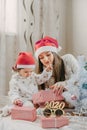 Boxing day. Little baby girl and mom unpack pink gift boxes near the Christmas tree. The kid touches bright Christmas-tree Royalty Free Stock Photo