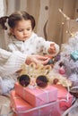 Boxing day. Little baby girl and mom unpack pink gift boxes near the Christmas tree. The kid touches bright Christmas-tree Royalty Free Stock Photo