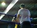 A boxing trainer / coach standing next to a boxing ring quickly bless and administer to the Thai boxing fighter before the match