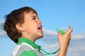 Boy, against blue sky, plays with whistle