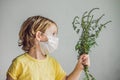 The boy is allergic to ragweed. In a medical mask, he holds a ragweed bush in his hands. Allergy to ambrosia concept. Royalty Free Stock Photo