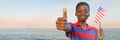 Boy with american flag giving thumbs up against water and evening sky Royalty Free Stock Photo