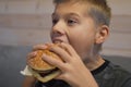 Boy with appetite eats delicious hamburger. child bites off large piece of sandwich