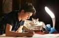 Boy architect student working on drafting project in night with cat in box beside Royalty Free Stock Photo