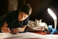 Boy architect student working on drafting project in night with cat in box beside Royalty Free Stock Photo
