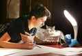 Boy architect student working on drafting project in night with cat in box beside Royalty Free Stock Photo