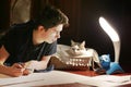 Boy architect student working on drafting project in night with cat in box beside Royalty Free Stock Photo