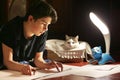 Boy architect student working on drafting project in night with cat in box beside Royalty Free Stock Photo
