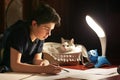 Boy architect student working on drafting project in night with cat in box beside