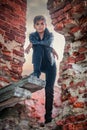 Boy of athletic build in black leather jacket stands on ruined brick wall