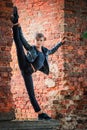 Boy of athletic build in black leather jacket stands on ruined brick wall