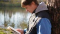 Boy in autumn Park near the lake reading a book. A beautiful autumn landscape. School education