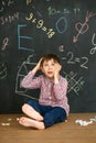 A boy on the background of a blackboard solves a difficult task. Sits with crayons and scratches his head