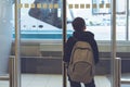 A boy with a backpack stands near glass door at the airport waiting transfer bus to the plane. Departure hall
