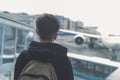 A boy with a backpack stands near glass door at the airport waiting transfer bus to the plane