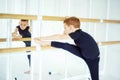 Boy ballet dancer doing exercise and stretching on ballet barre near mirror in white light ballet studio. Dancing boy. Activity