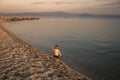 Boy on the beach. concept of loneliness. Cute child waving hand at seashore in evening. Boy sits in sea water, rear view