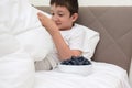 A boy in a bed eating fresh tasty blueberry from a wnite ceramic bowl for breakfast