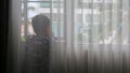 a boy behind the curtain is looking at the view in the window Royalty Free Stock Photo
