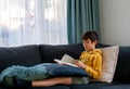 A boy concentrate on reading the book on the couch in free time