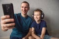 A boy in big headphones is sitting next to his dad, making a video call on the phone Royalty Free Stock Photo