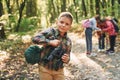 Boy with binoculars standing in front of his friends. Kids in green forest at summer daytime together