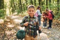 Boy with binoculars standing in front of his friends. Kids in green forest at summer daytime together