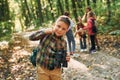 Boy with binoculars standing in front of his friends. Kids in green forest at summer daytime together