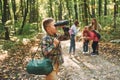 Boy with binoculars standing in front of his friends. Kids in green forest at summer daytime together