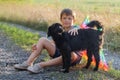 boy with black dog. boy sits on road and hugs dog. Animal on background of wild grass in the field. Walk with your pet