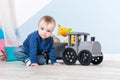 Boy blond in a blue sweater sits on a wooden floor. One year old baby playing with wooden toys.  train made of wood, with girafe Royalty Free Stock Photo