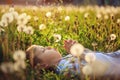 Cute boy blowing on dandelion lying on grass in sunny clear day