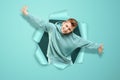 Boy on a blue background, happy waving his hands, punching a paper wall