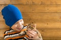 Boy in a blue hat holds a small kitten, against a wooden wall