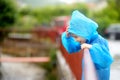 A boy in a blue raincoat watching of water flow in river during pouring rain while walking. Children love to run and play in rainy Royalty Free Stock Photo