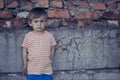 A boy with blue, sad, eyes stands leaning against a brick wall, looking at the camera. Portrait of a beautiful baby. Royalty Free Stock Photo