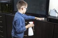 Boy in a blue shirt and glasses cleans the room. He wipes dust with a white cloth.