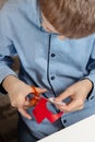 Boy in a blue shirt and glasses sits at a desk and concentrates on doing plastic work with colored paper. The boy is painting