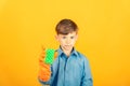 A boy in a blue shirt and orange gloves is holding a green washing sponge on a yellow background Royalty Free Stock Photo