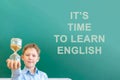 A boy in a blue shirt stands at a blackboard that says It`s Time To learn English