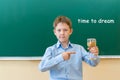 A boy in a blue shirt stands at a Board that says, time to dream. he holds an hourglass in his hand and points at it