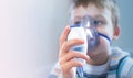 A boy in a blue T-shirt holds an inhalation mask near his face. The child treats colds, coughs at home. Free space for