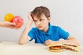 Boy in blue at the table chooses between fastfood and fruits