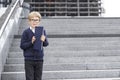 A boy in a blue uniform and glasses stands on the steps with a blue notebook