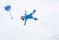 boy in blue winter suit cleared snow after blizzard and lay down on snow to rest, with a large shovel nearby Royalty Free Stock Photo