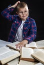 A boy with books sits at the table. Smiling fat schoolboy with glasses. Back to school. Black background. Vertical
