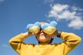 boy in a bright yellow sweater holds two knitted plush yellow-blue hearts in front of his eyes against blue sky